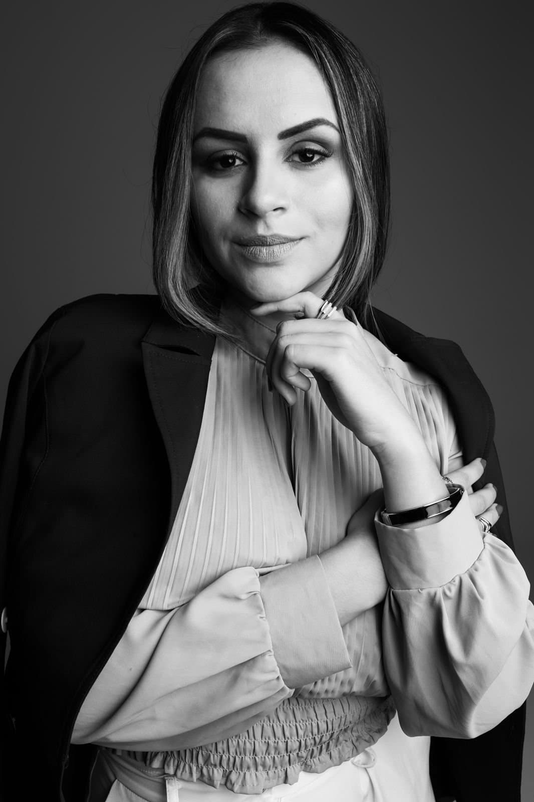 Retrato em preto e branco da Dra. Mariane de Andrade Fagundes, de blazer escuro sobre blusa clara, com a mão junto ao queixo.